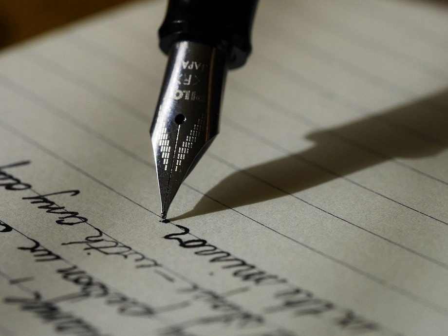 Pluma escribiendo sobre un cuaderno para los concursos literarios de diciembre